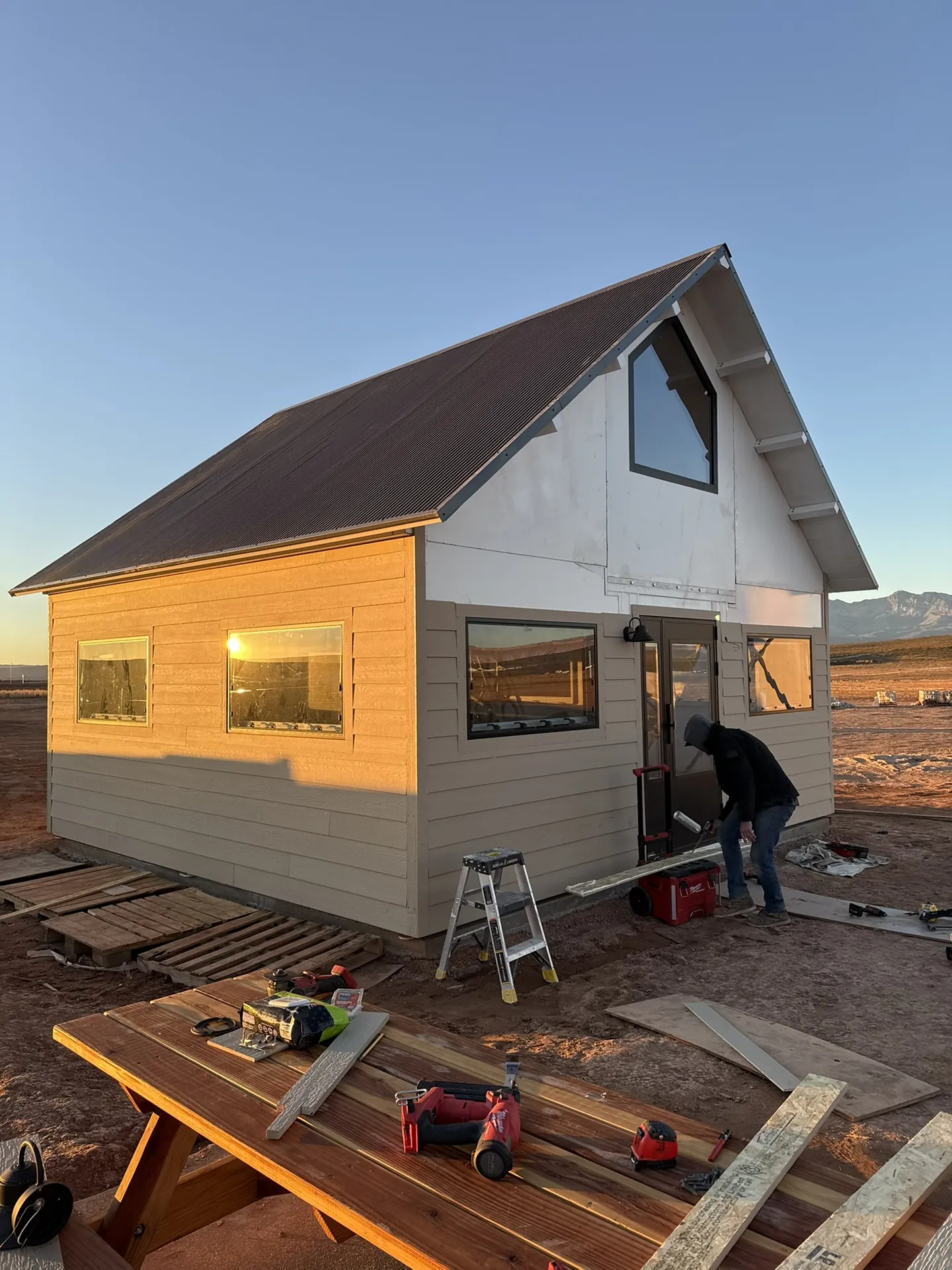 Early progress on the Boxabl siding project at Liberty Village — golden hour, worker at front door