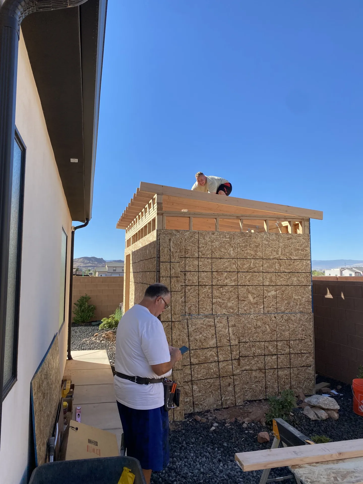 Viking Solutions shed build — crew member on roof framing with second crew member below, mountains visible