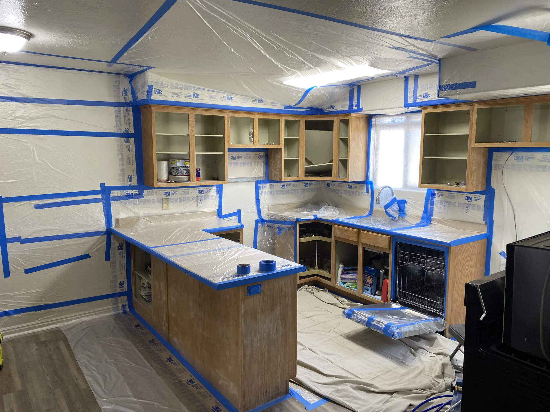 Kitchen fully masked with blue tape and plastic sheeting before cabinet spray painting