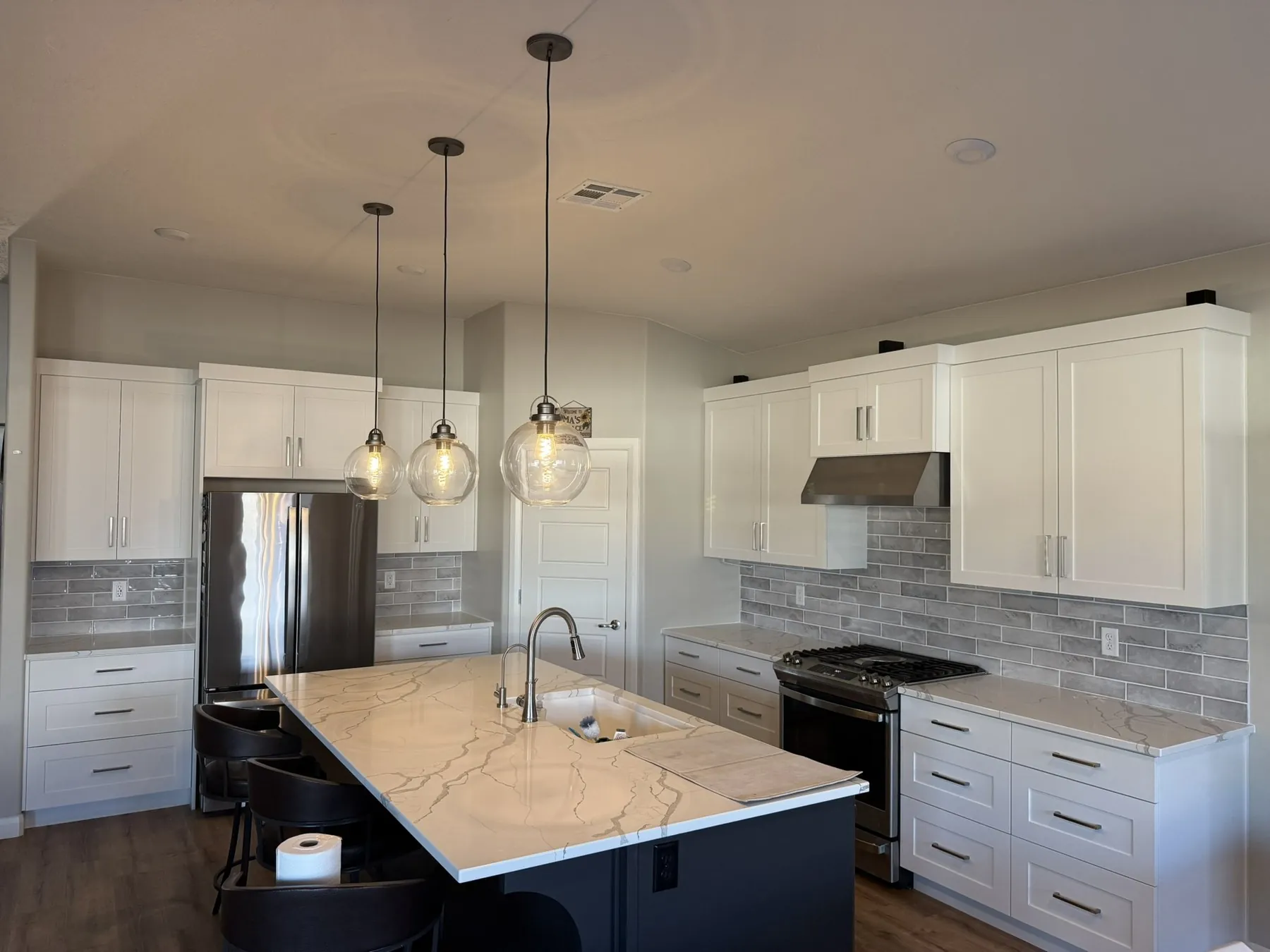 Finished kitchen backsplash — gray subway tile, white shaker cabinets, quartz island, pendant lights