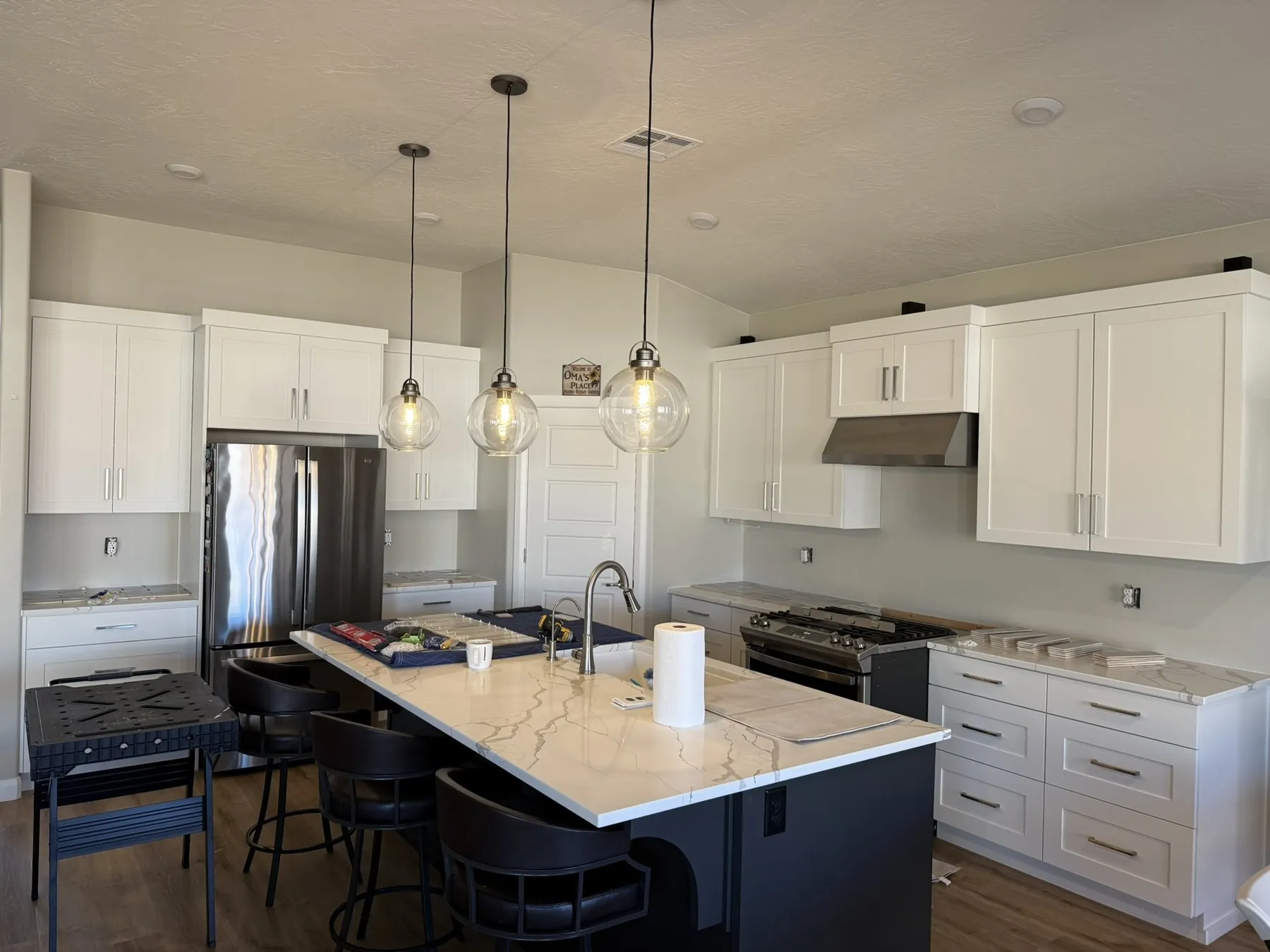 Kitchen during backsplash installation — tile supplies on island, white shaker cabinets, quartz countertops