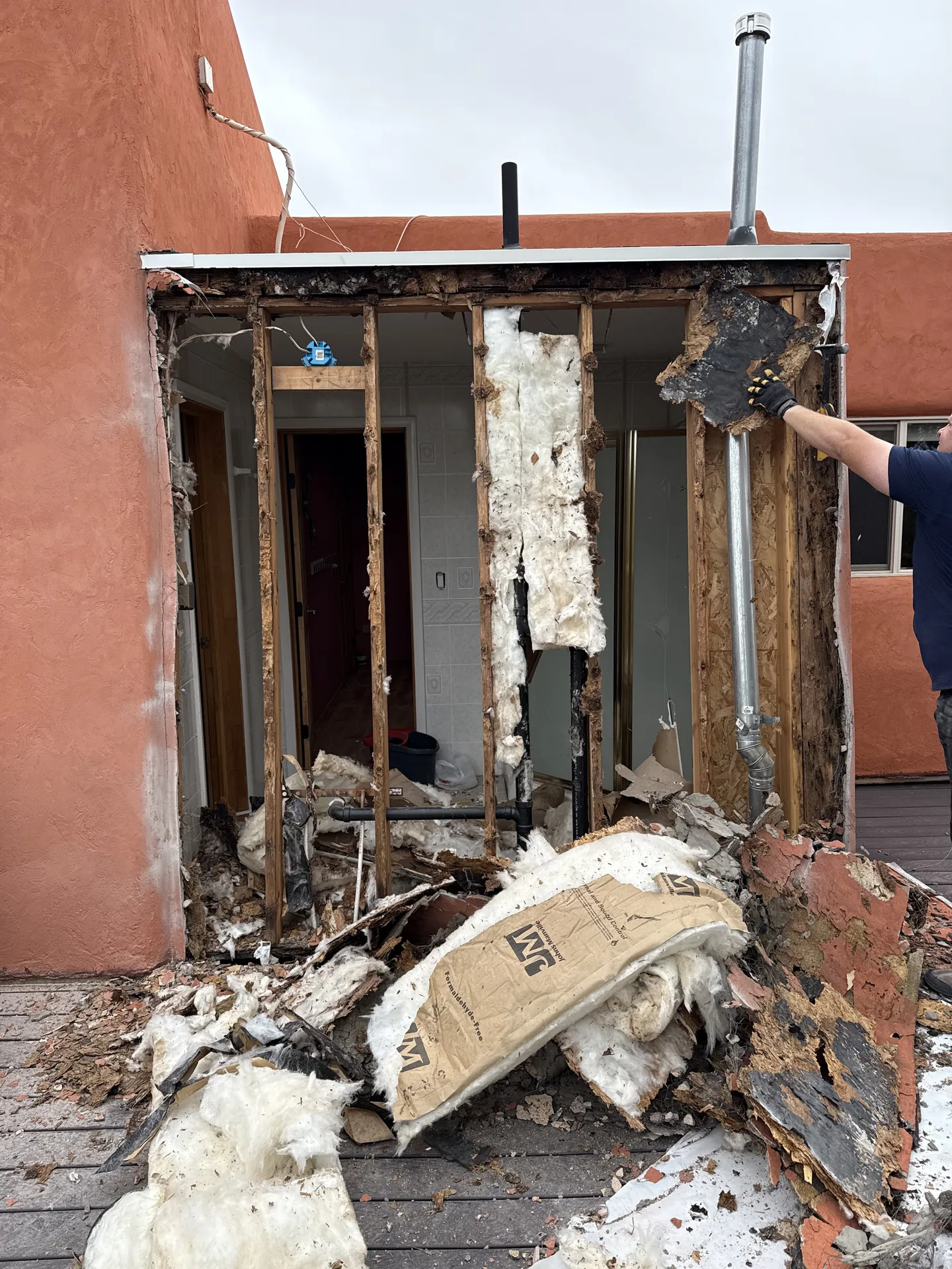Structural bathroom remodel — exterior wall completely removed from outside, adobe stucco home, debris pile, open framing visible