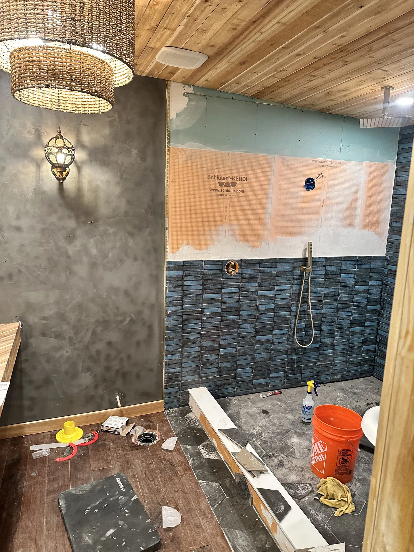 Bathroom remodel progress — Schluter-KERDI waterproofing membrane on upper walls, blue teal tile installed on lower half, freestanding tub in place