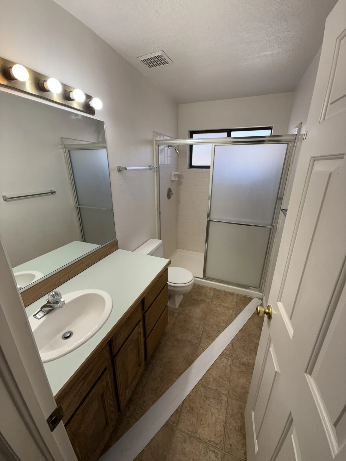 Condo before remodel — master bathroom with original oak vanity, frosted glass shower door, and dated tile