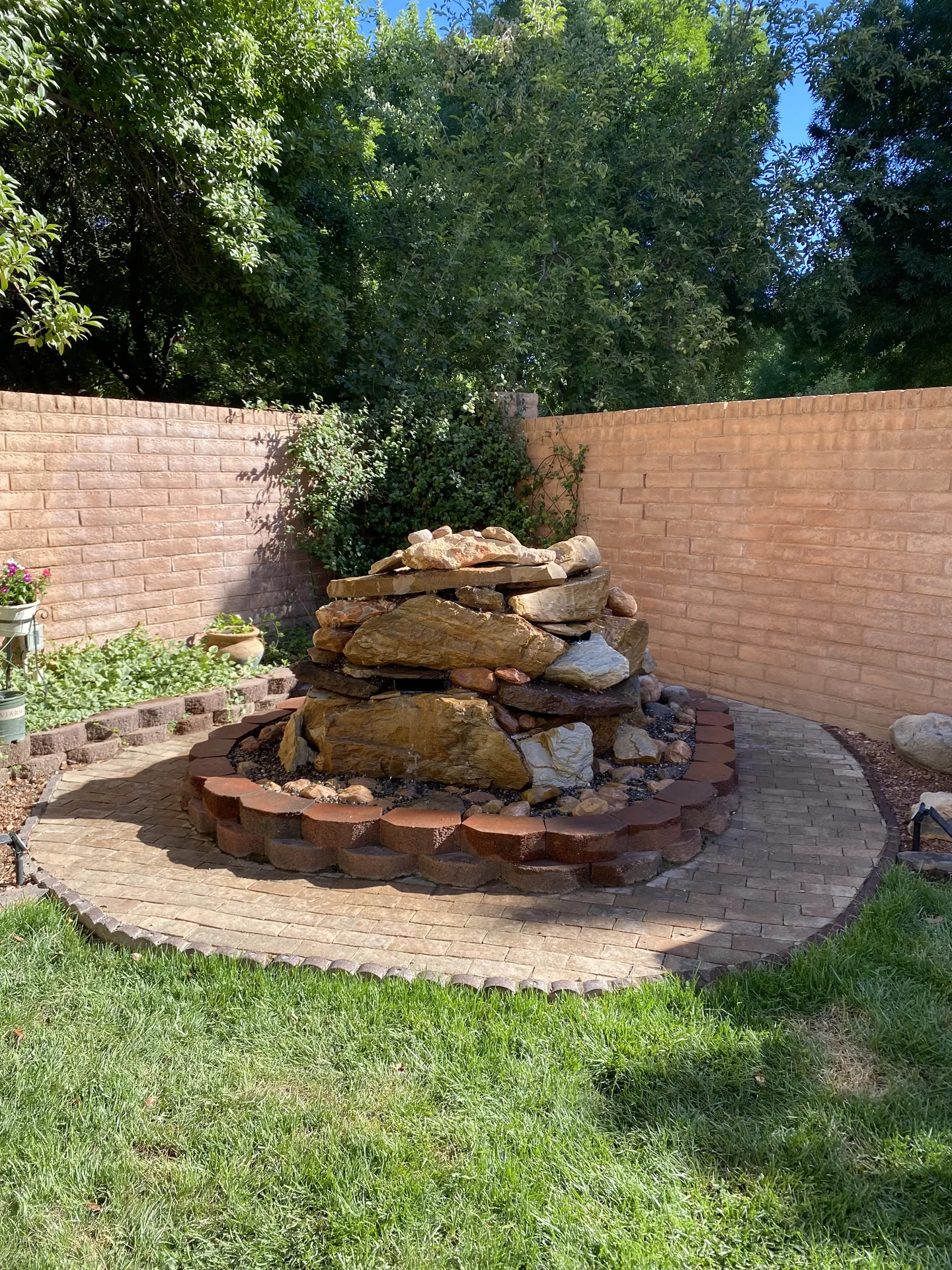 Close-up of finished stacked sandstone fountain — boulder detail, paver border, and black river rock fill