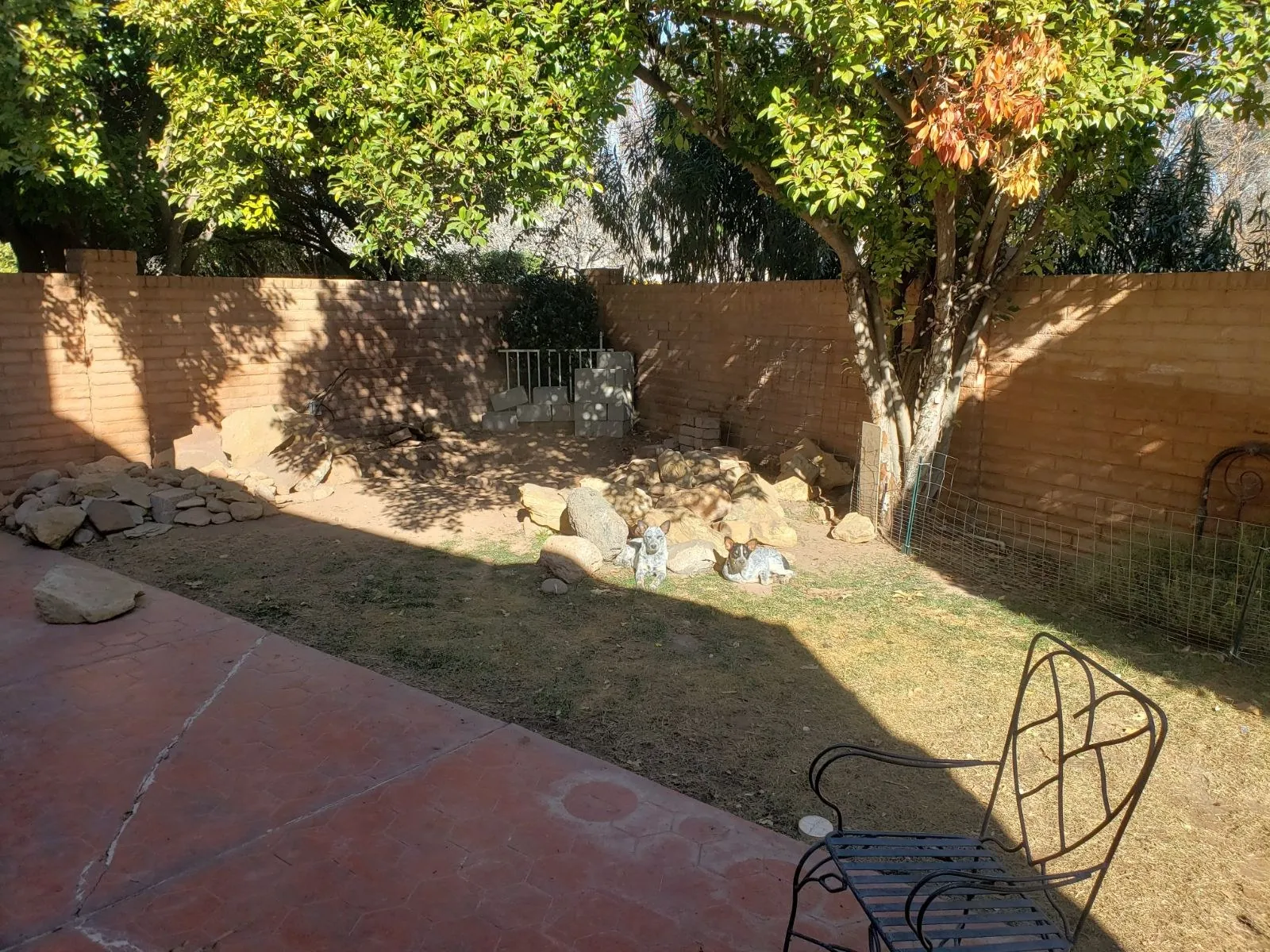 Before — neglected backyard corner with loose sandstone rocks and concrete figurines against a block wall in St. George, Utah