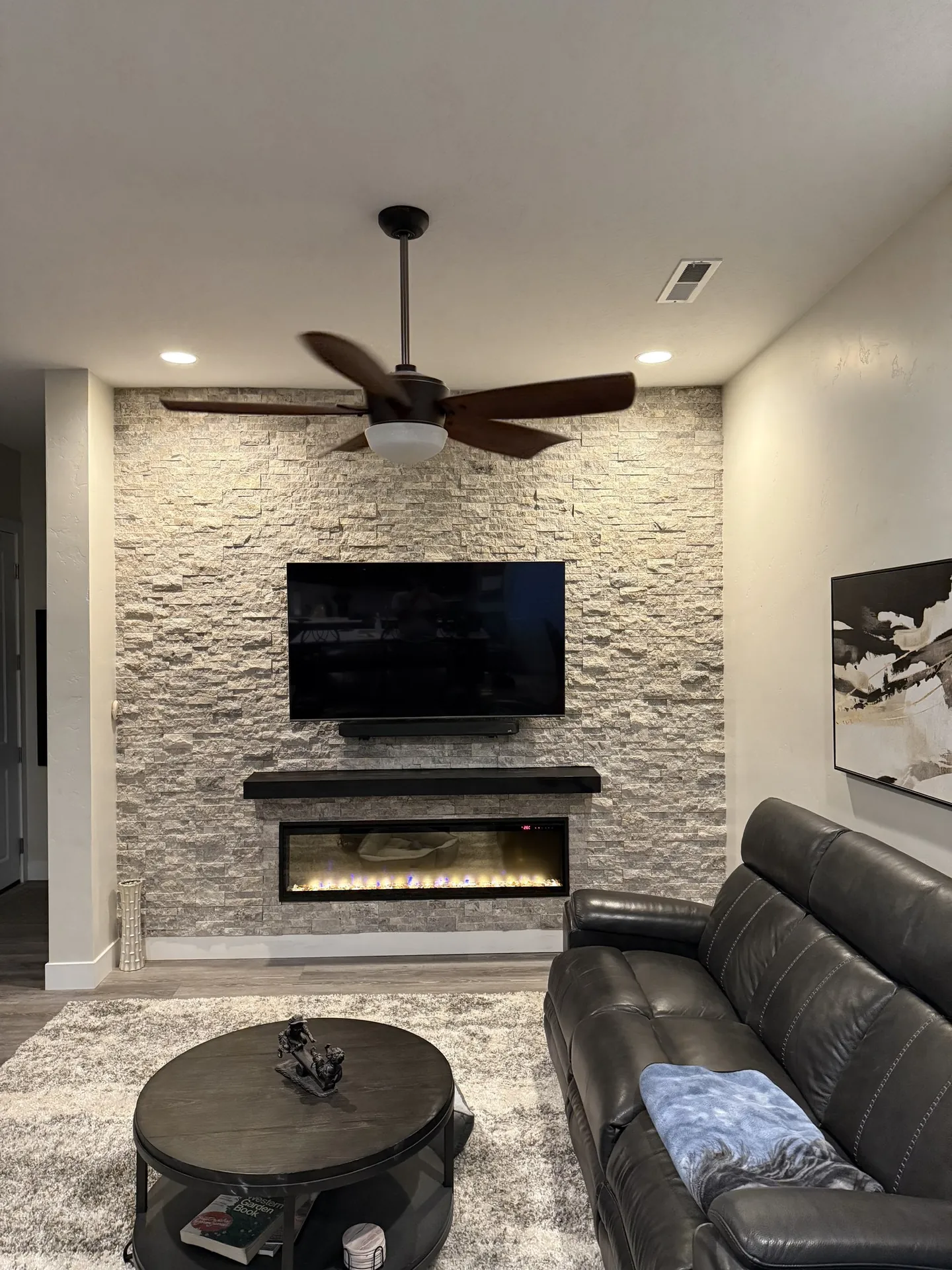 After: stacked ledger stone fireplace wall with linear electric insert and TV — fireplace lit