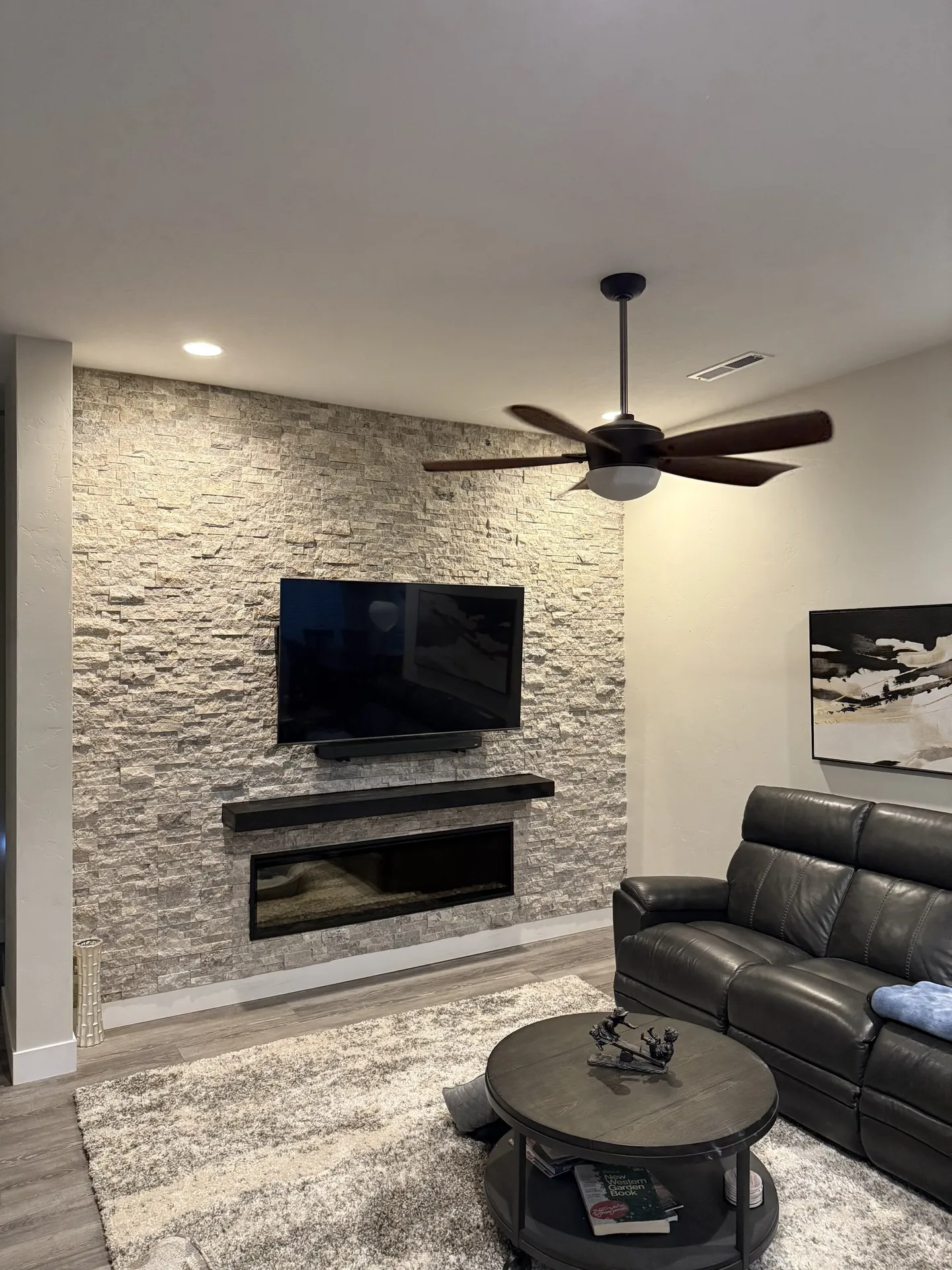 Stacked ledger stone fireplace wall — full living room view with leather sofa and ceiling fan