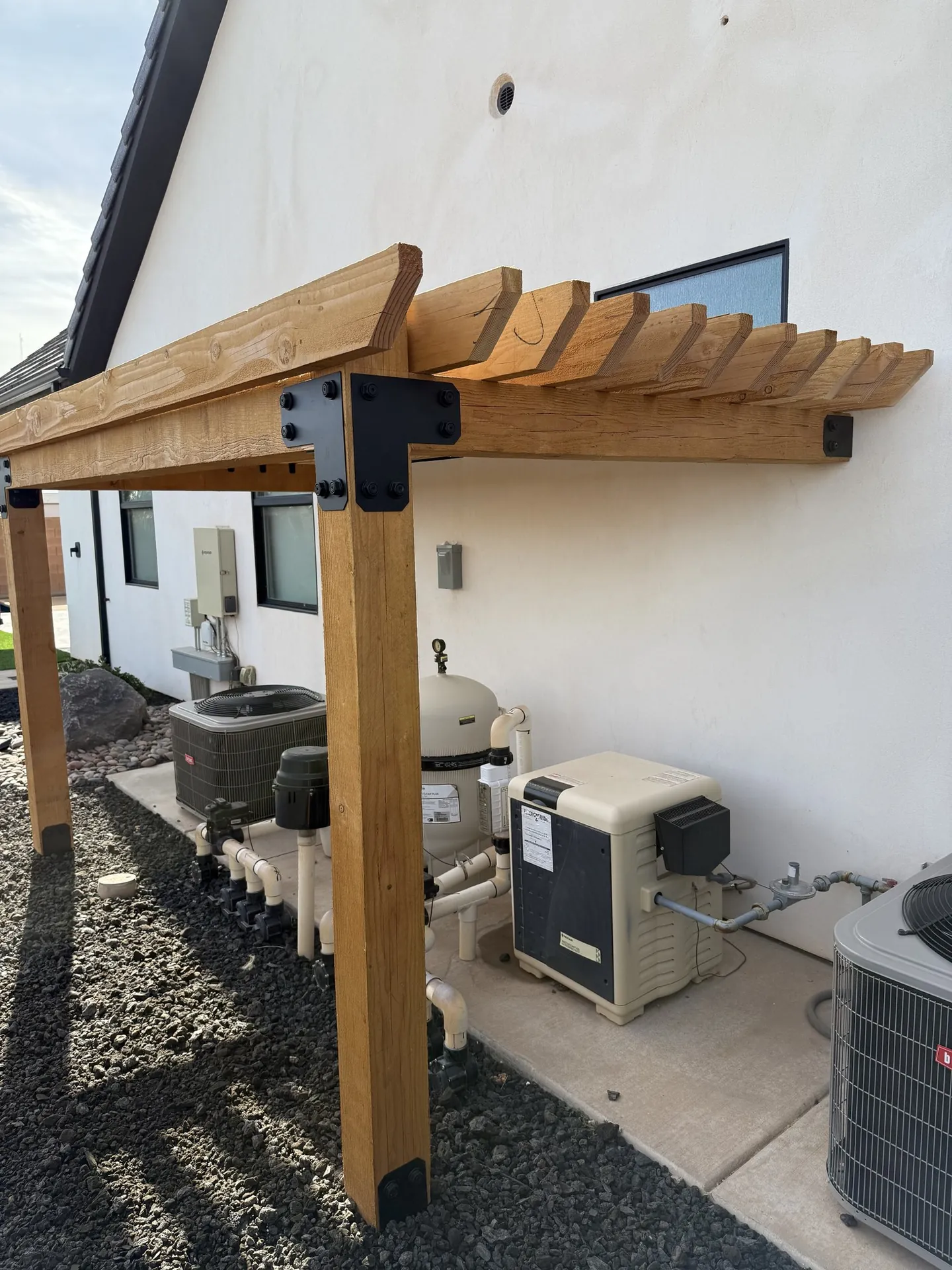 Close-up of black powder-coated steel post base and beam bracket hardware on cedar pergola