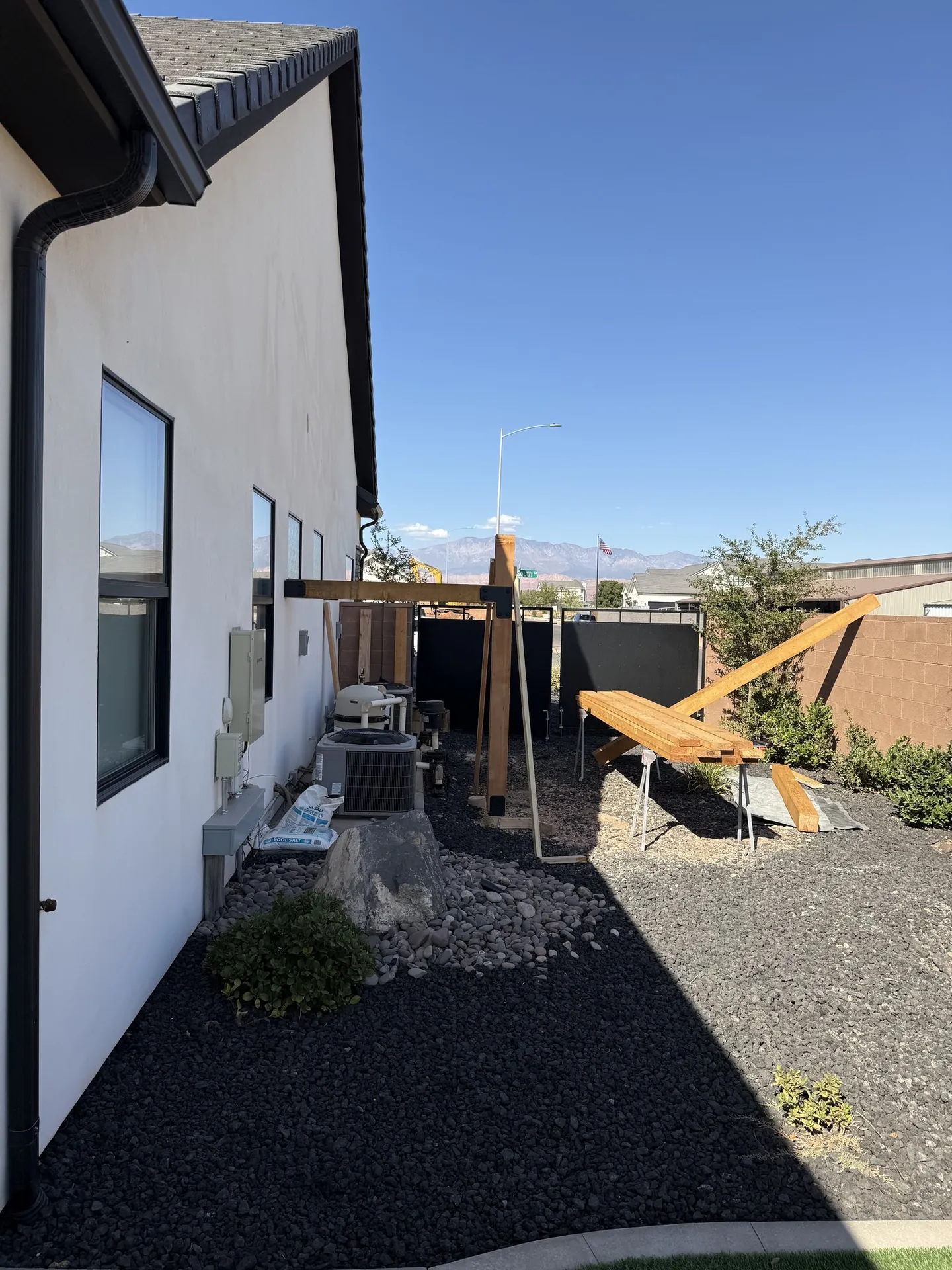 Pool equipment pergola mid-construction — posts standing, beams being assembled on sawhorses with mountains visible in background