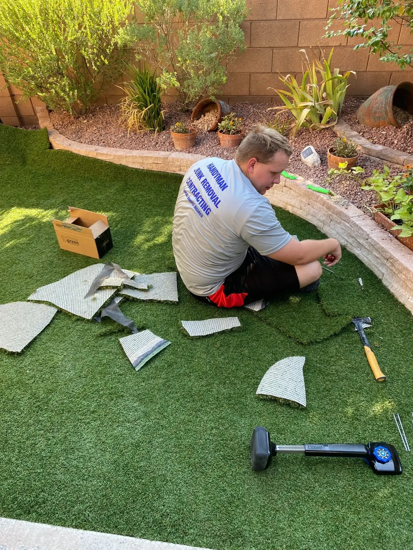 Viking Solutions crew member trimming artificial turf seam by hand — precision cut along curved retaining wall border